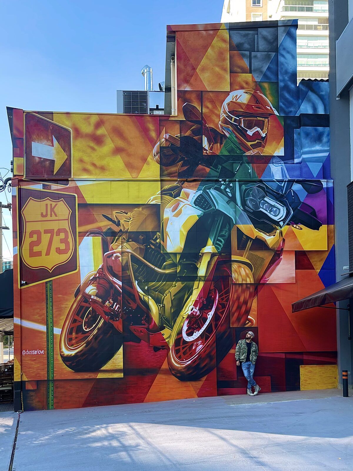 Mural de grande formato com motociclista e moto em cores quentes.